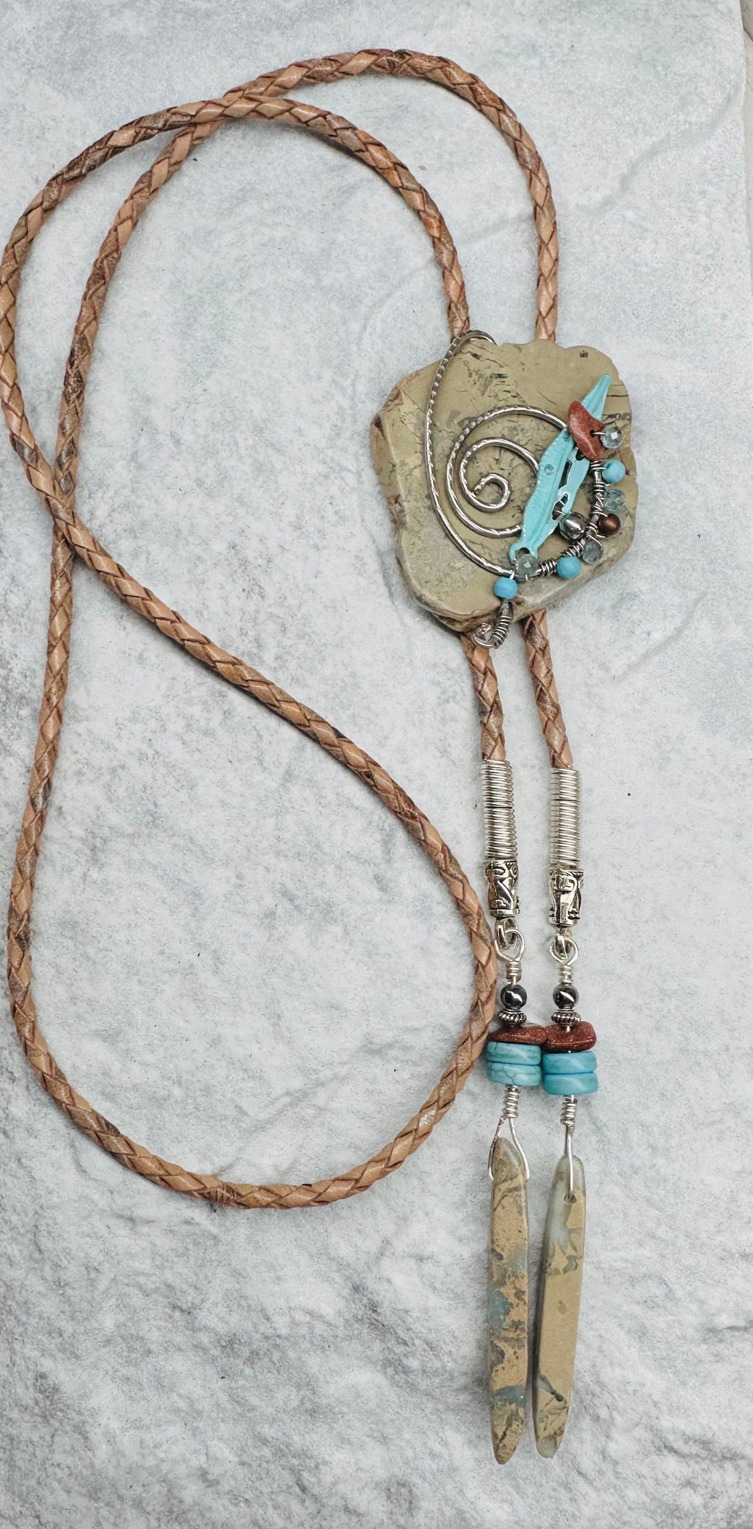 A beaded bolo tie with a Snakeskin Jasper pendant, wire-wrapped, with a braided leather base and bead detailing, accompanied by matching earrings with Snakeskin Jasper beads.